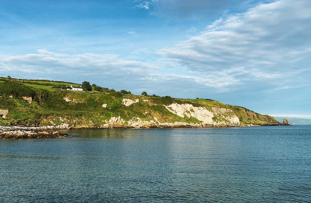 Green cliffs and rocky shore along the Islandmagee coast under a bright sky