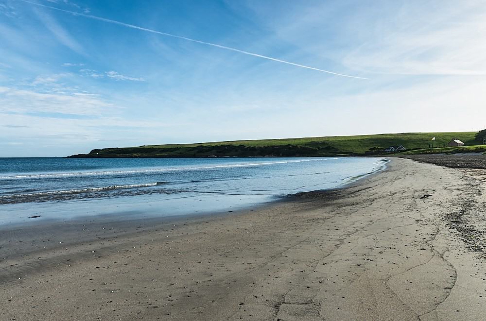 The sheltered horseshoe of golden sand at Browns Bay, Islandmagee, with a green headland curving round the calm bay under a bright blue sky
