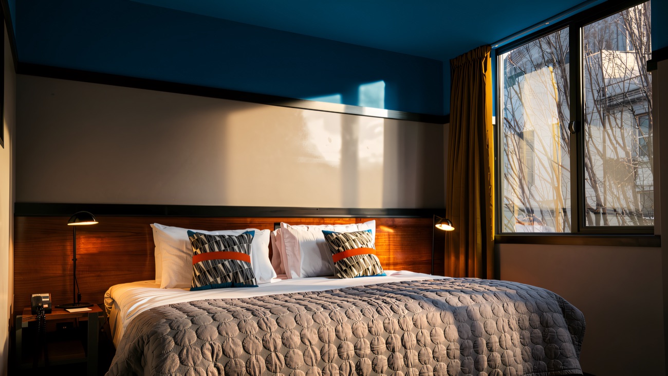 A guest room with a teal ceiling, timber headboard and daylight through the tall window