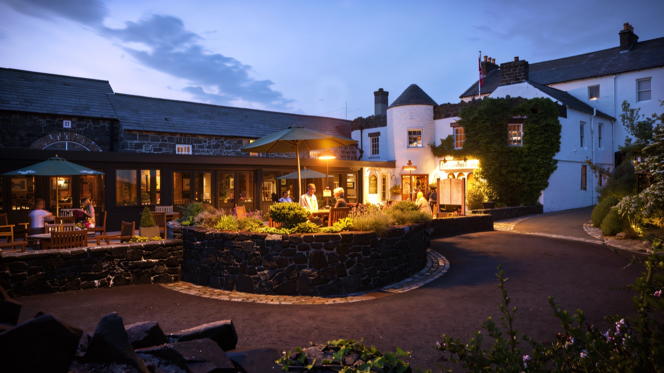 The Bushmills Inn at dusk, its windows glowing warm across the flagstone courtyard and the little round turret catching the last light