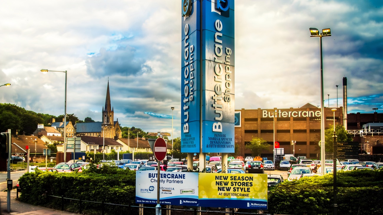The tall blue Buttercrane Shopping totem signs beside the multi-storey car park, with Newry Cathedral's spire in the background