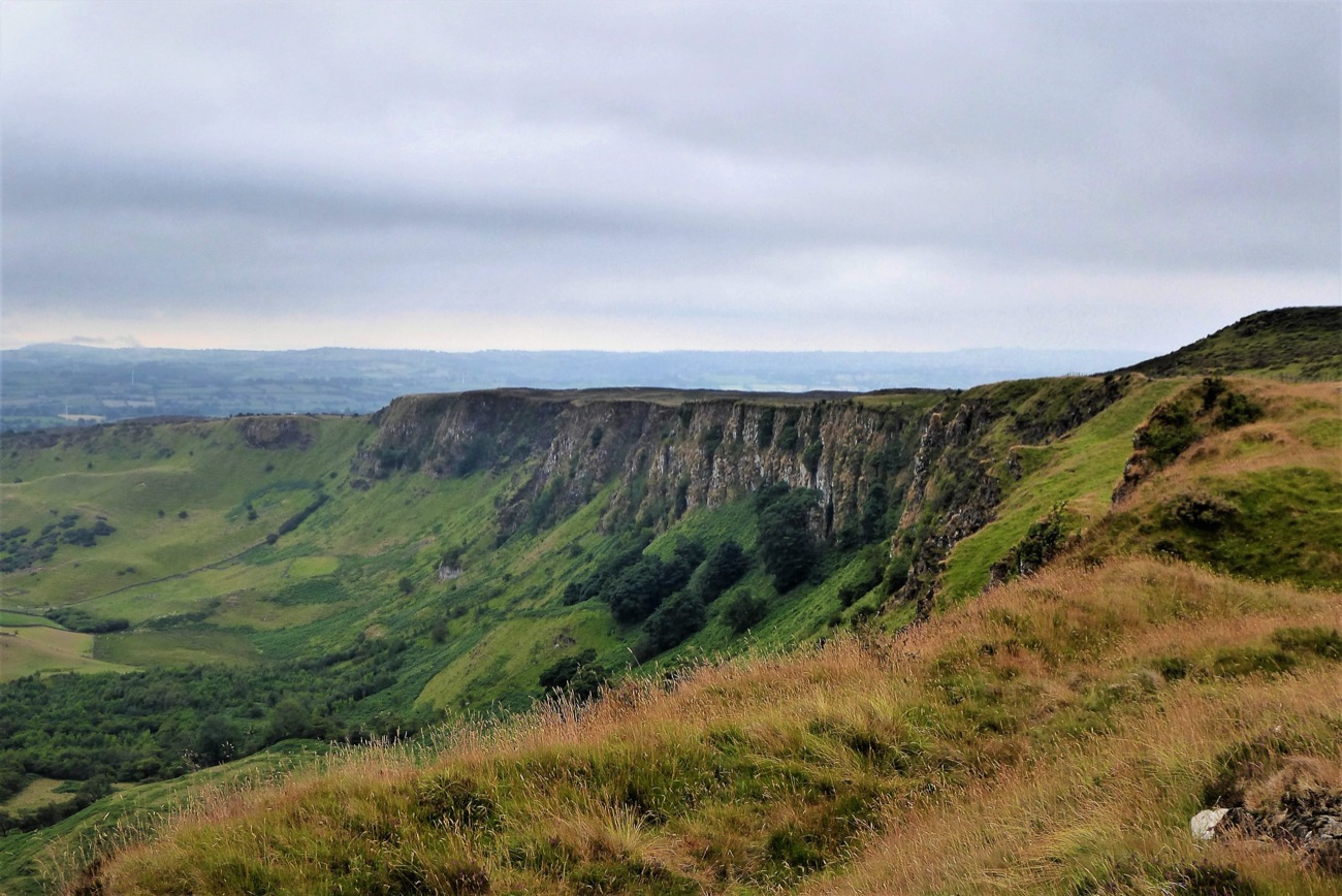 The curving cliff face of the Knock Dhu escarpment above a green glen near Cairncastle