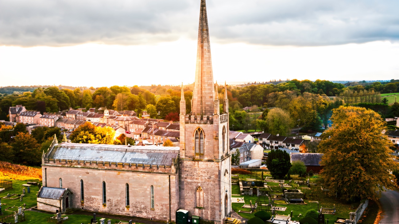 The parish church and its tall spire seen from above, set among the rooftops and the wooded demesne.