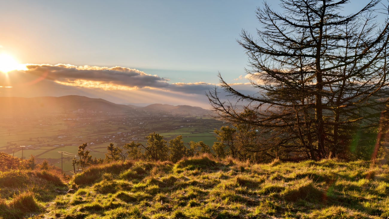 Low golden light spills over the valley from the slopes above the lake.