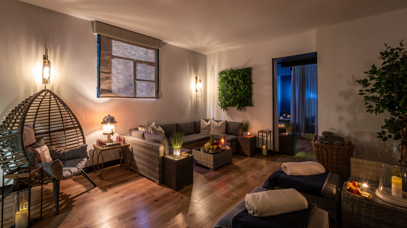 The spa relaxation lounge — soft lamplight, candles, a hanging chair and warm towels stacked ready.