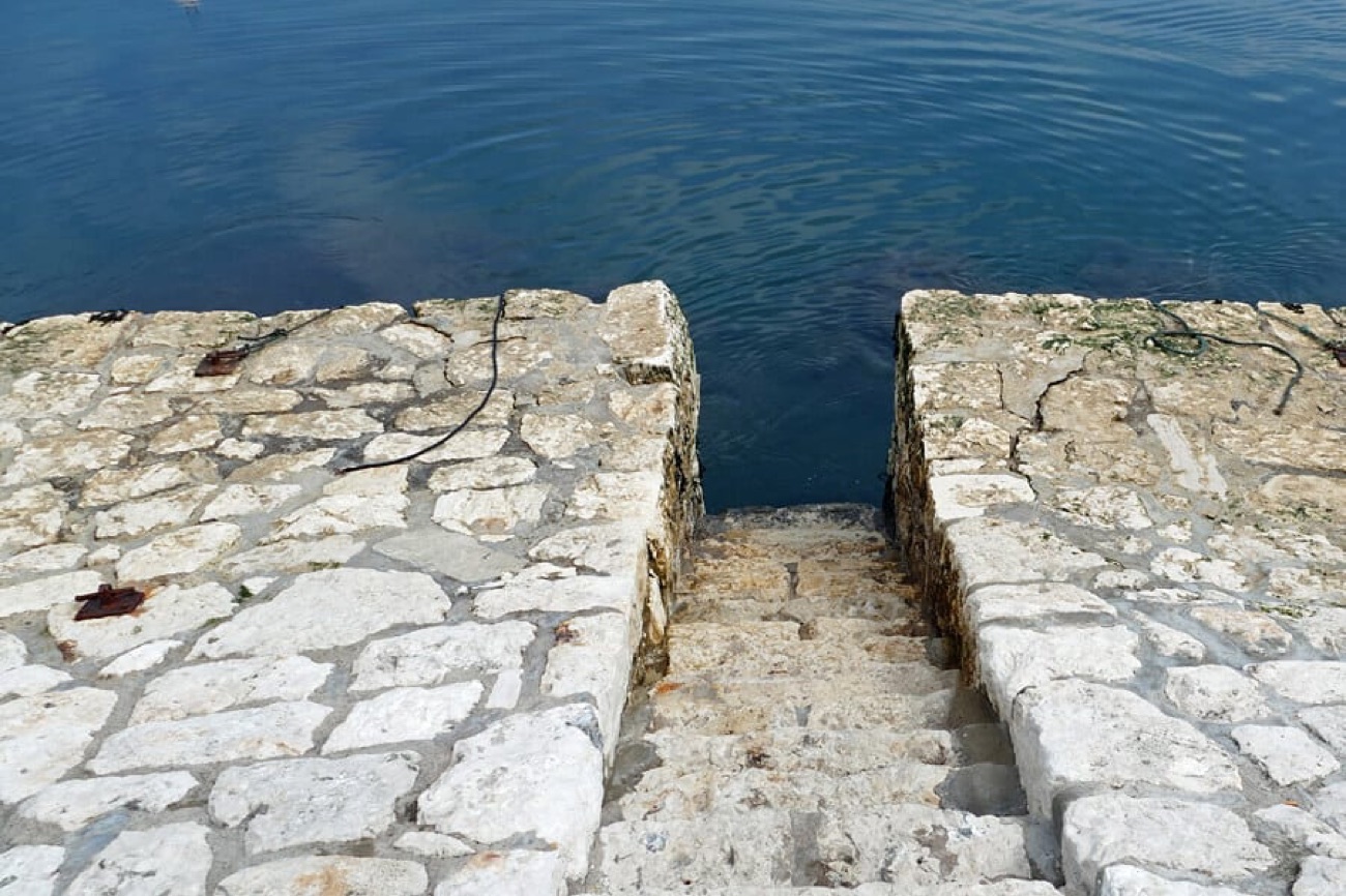 The old stone harbour steps at Carnlough leading down into clear green water — the spot used as the Braavos canal in Game of Thrones