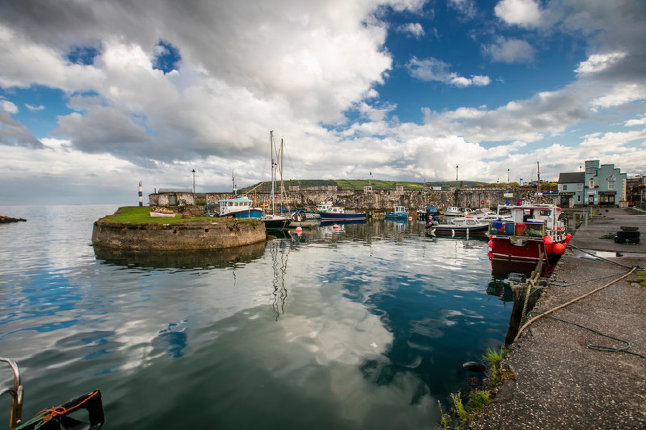 Fishing boats moored in Carnlough harbour with a dramatic cloudy sky mirrored in the calm water