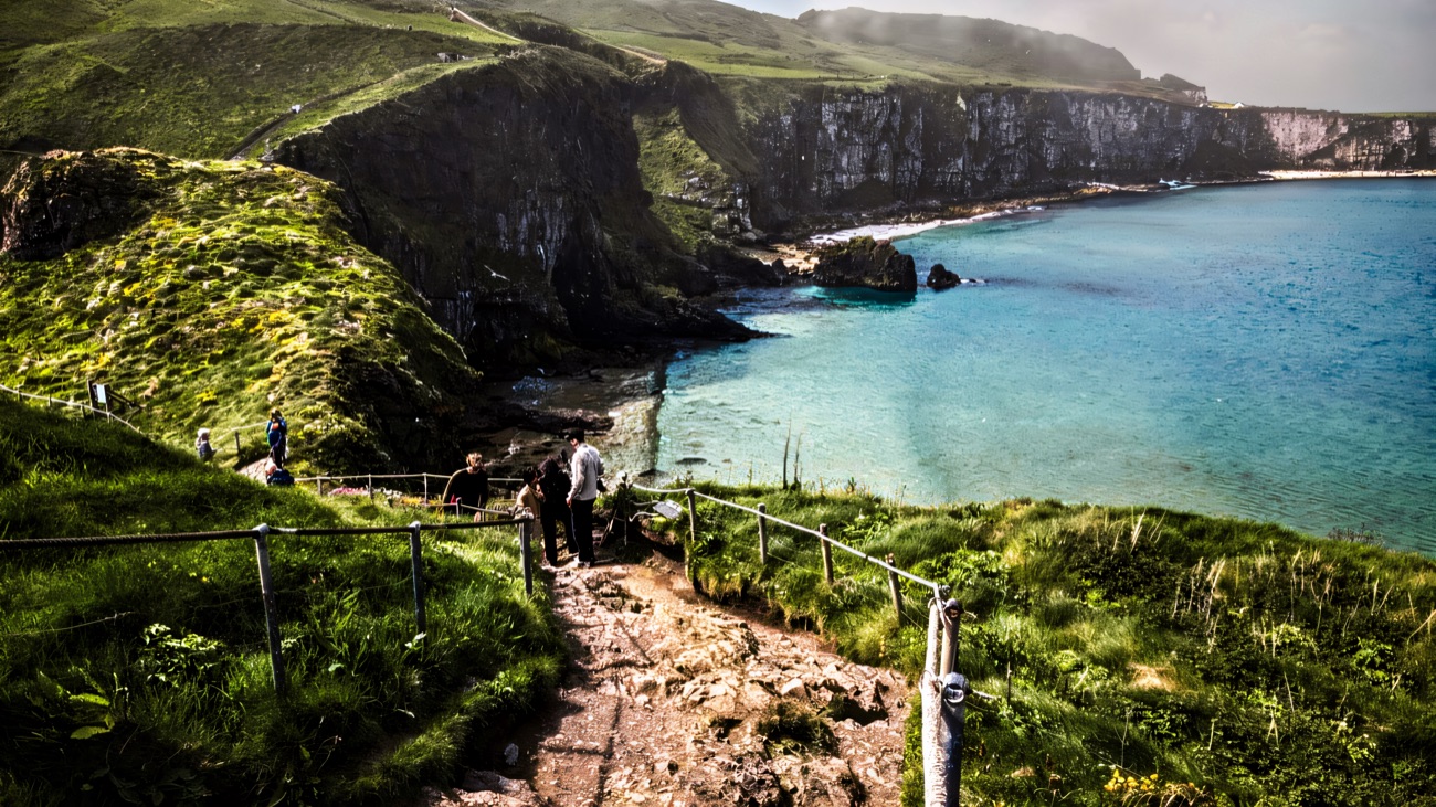 The clifftop coastal path descending towards the bridge with a turquoise bay below