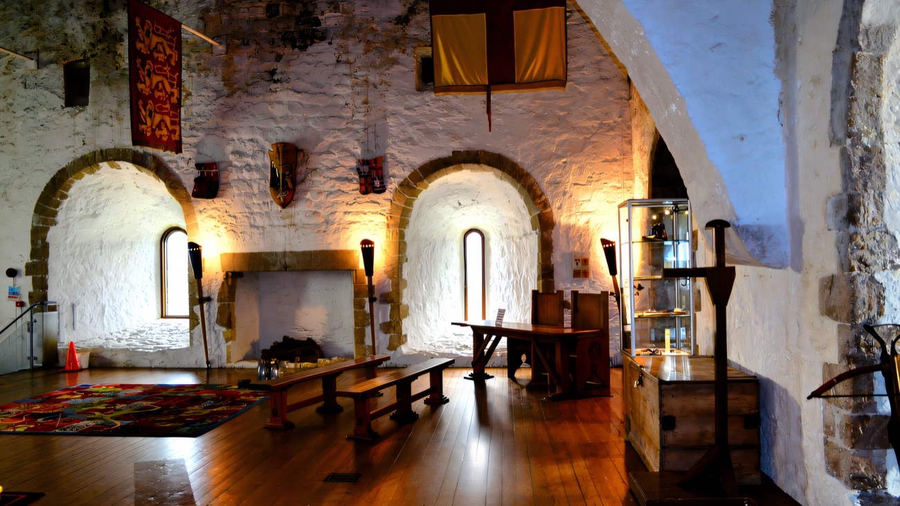 Inside the keep at Carrickfergus Castle — the restored banqueting hall with heraldic banners, a stone fireplace and whitewashed walls