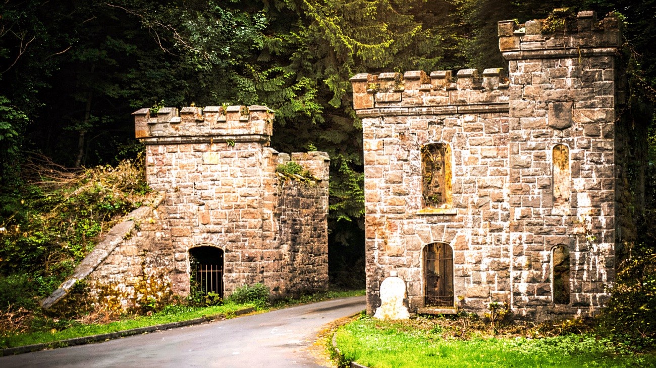 The two battlemented gatehouse towers of Castle Caldwell in grey stone beside the forest road