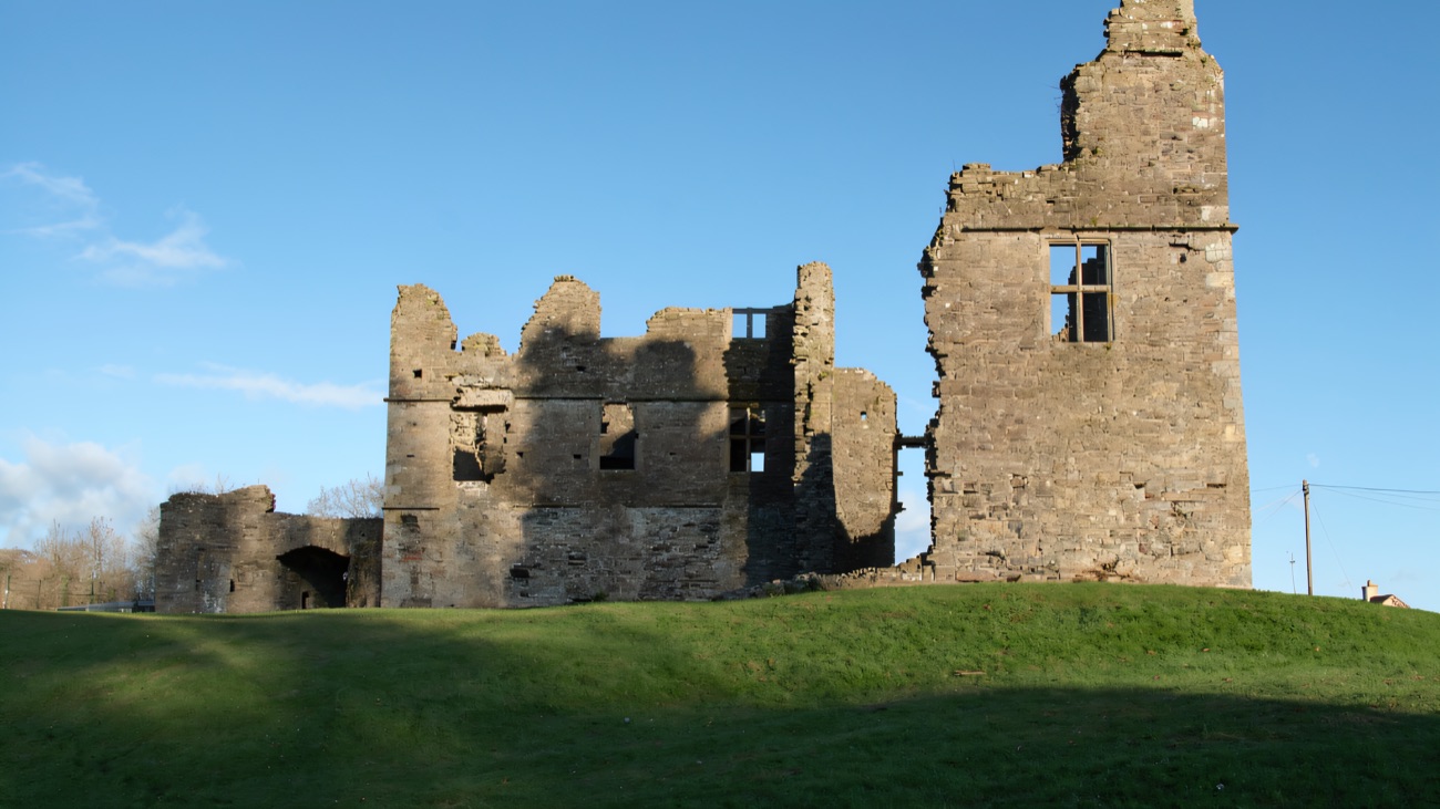 The ruined Jacobean manor house of Castle Caulfield standing on its green mound under a blue sky, with the gatehouse arch to the left