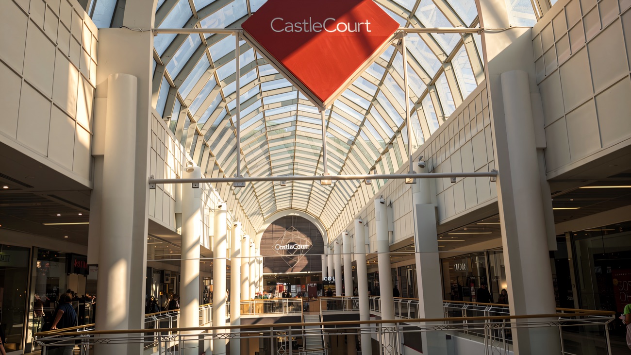 The white glass barrel-vault atrium inside CastleCourt, with the red CastleCourt diamond sign hanging overhead