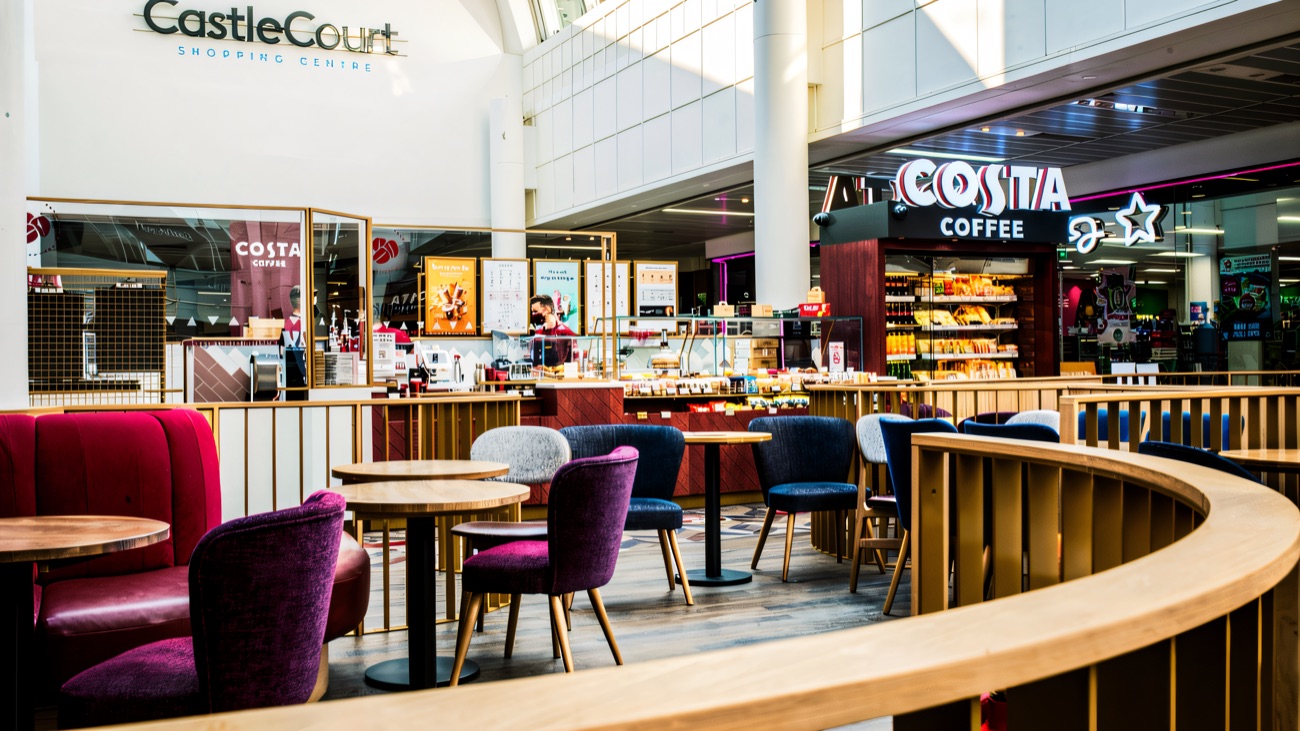 The food court seating area at CastleCourt with colourful chairs, the CastleCourt sign on the wall and Costa Coffee behind