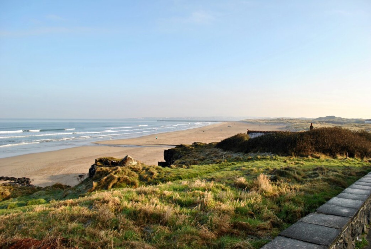The long strand at Castlerock in golden light, seen from the grassy promenade with the beach sweeping into the distance