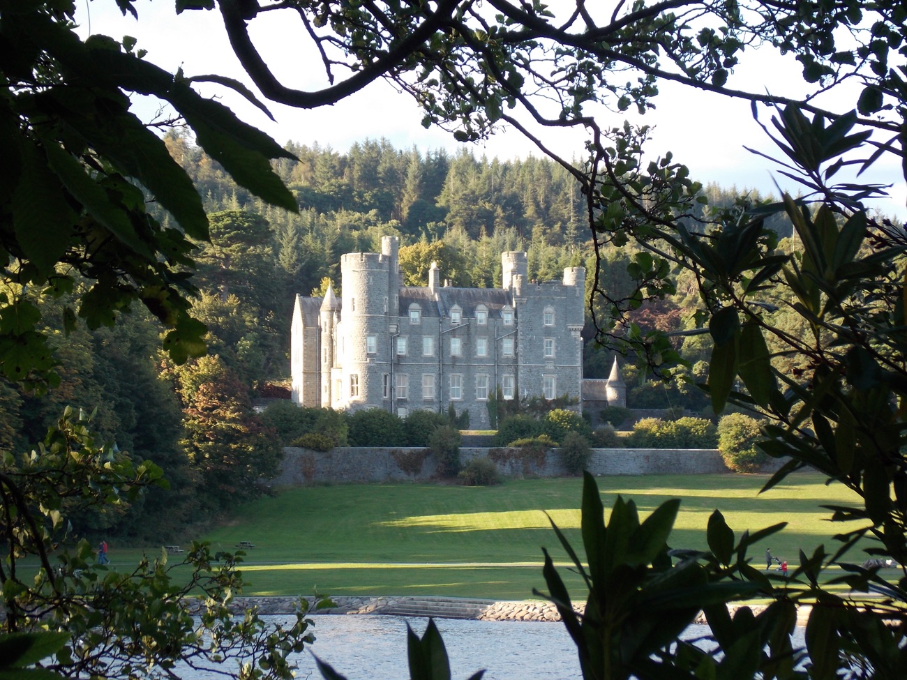Castlewellan Castle, a grey Scottish-baronial house framed by trees above a sweeping lawn