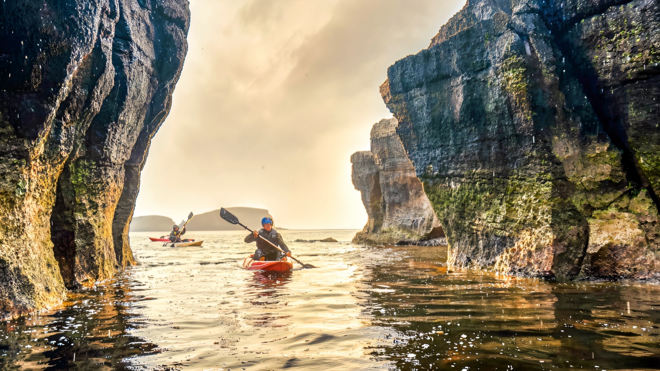 Threading between towering sea stacks, paddle dipping into glassy swell