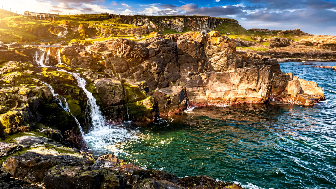 A little waterfall spills into a rugged cove on the Causeway coast