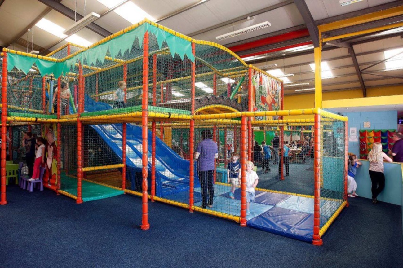 A wider view of the Cheeky Chimps play frame with its blue slides, ball-play area and the café seating visible beyond