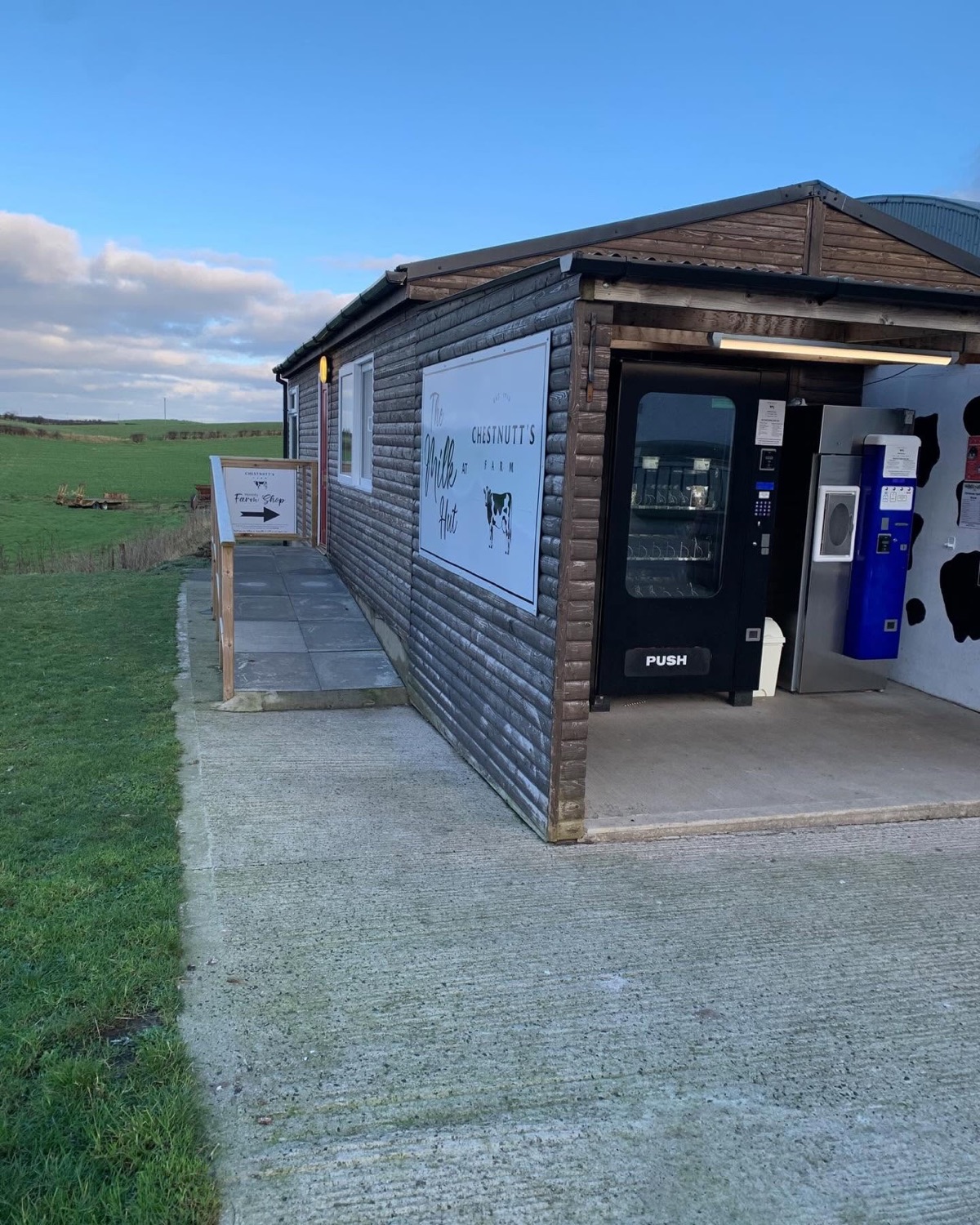 The Milk Hut at Chestnutt's Farm — the timber cabin with its self-service milk vending machines, Farm Shop sign and green Causeway Coast fields behind