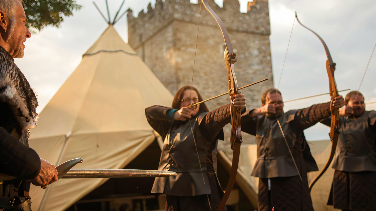 Costumed archers draw their bows with the Winterfell tower behind
