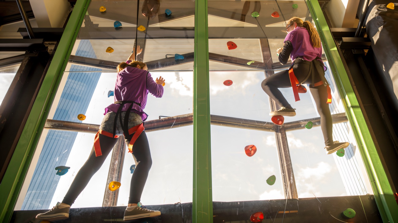 Climbers working their way up the coloured holds on the tall glass-backed wall