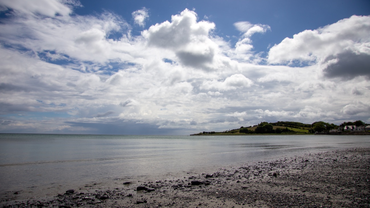 Cloughey Bay with dramatic clouds building over the headland and a pebbly foreshore in the foreground