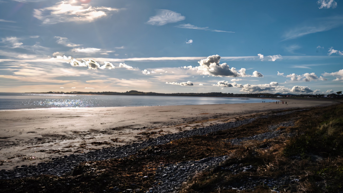 Shingle, seaweed and open sand stretching out at low tide on a bright day.