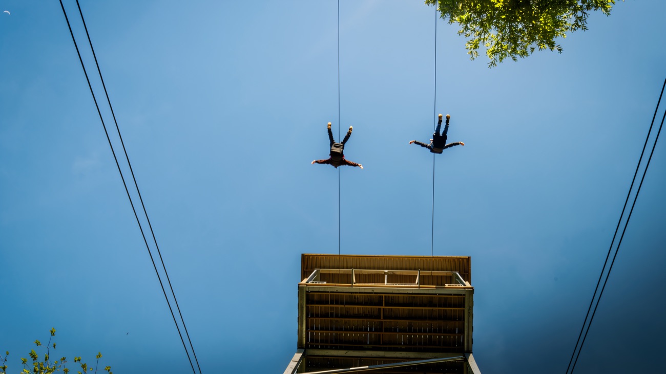 Two riders soar off the tower against a clear blue sky