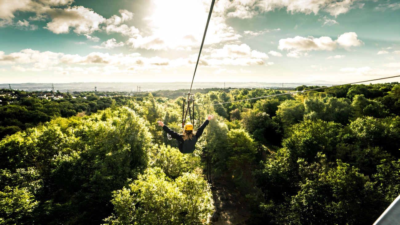 A zip line rider soaring out over the treetops of Colin Glen toward the Belfast skyline