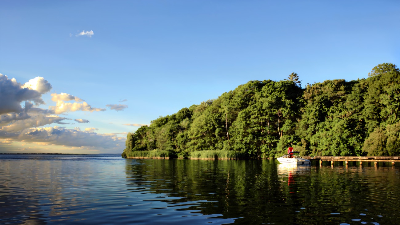 The wooded island rising from calm water, a boat moored beside the jetty