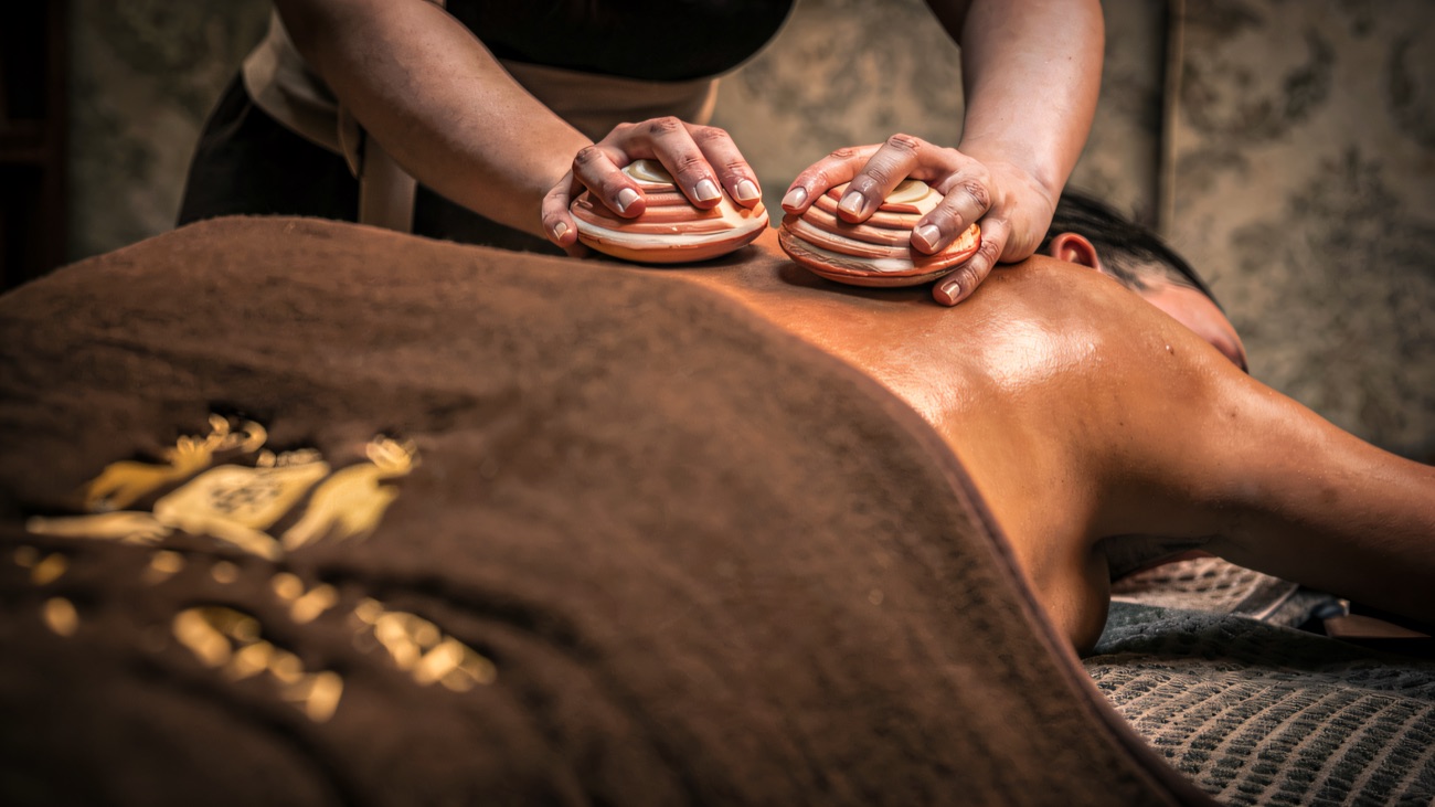 A therapist works through a warm-stone back treatment in a low-lit room.