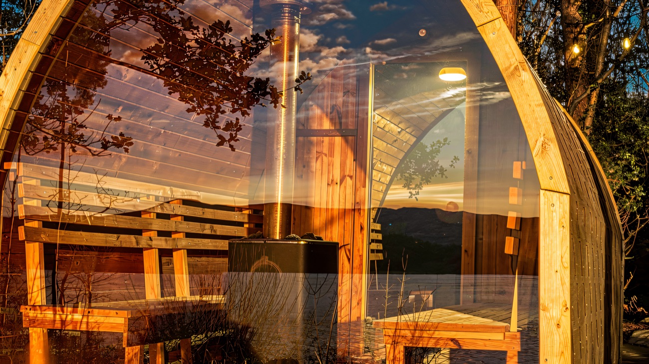 The sauna cabin lit up at golden hour, framed by trees above the shoreline