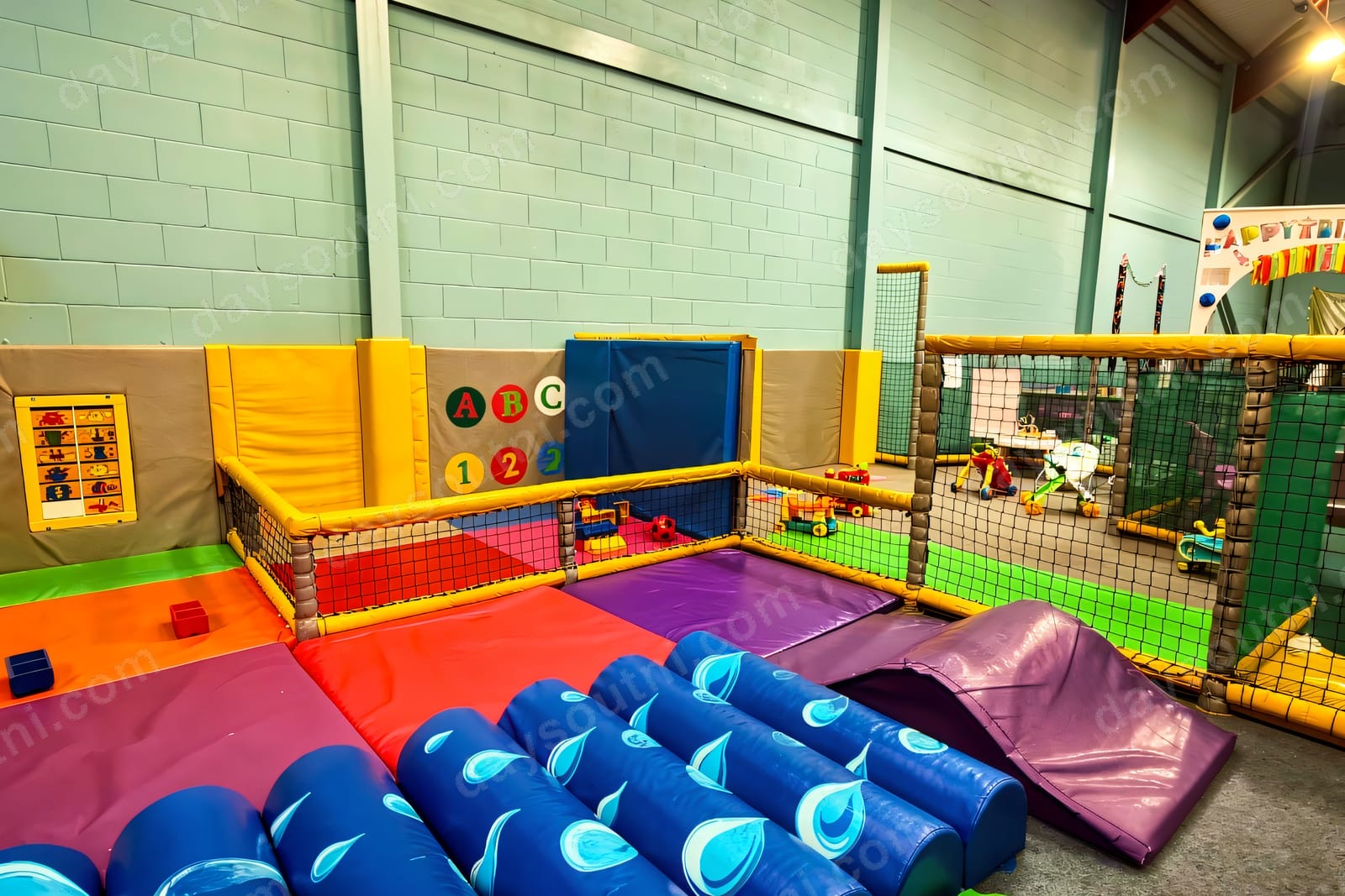The gated toddler soft play area at Cosmic Kids Cookstown, with padded blue rollers, an ABC/123 wall and a netted frame beyond