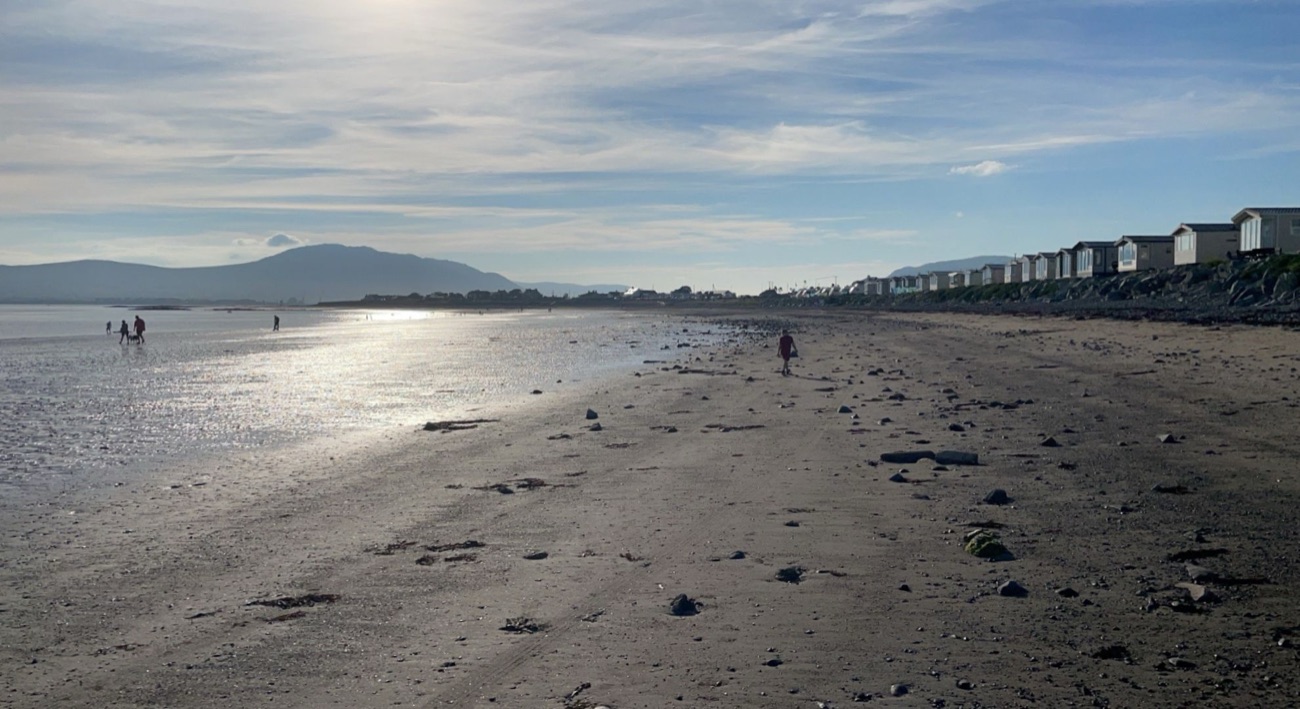 The wide flat sandy expanse of Cranfield Beach at low tide, backed by a line of caravans, with the Cooley Mountains on the horizon
