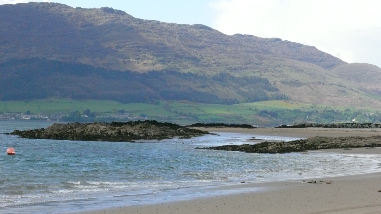 The Cooley Mountains rising steeply across the water from the sandy shore at Cranfield, a marker buoy in the shallows