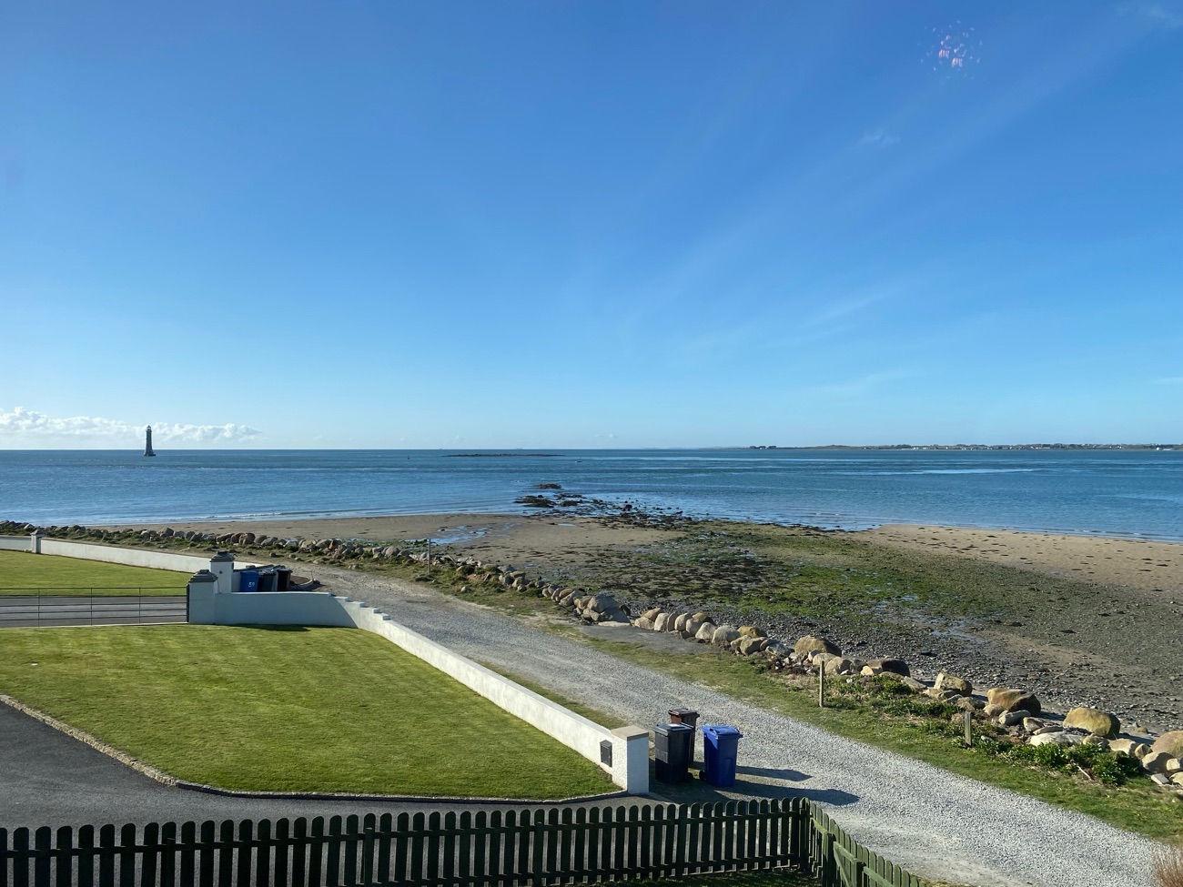 Calm, sheltered water at the mouth of Carlingford Lough seen from Cranfield, with the Haulbowline Lighthouse out in the channel and a grassy foreground