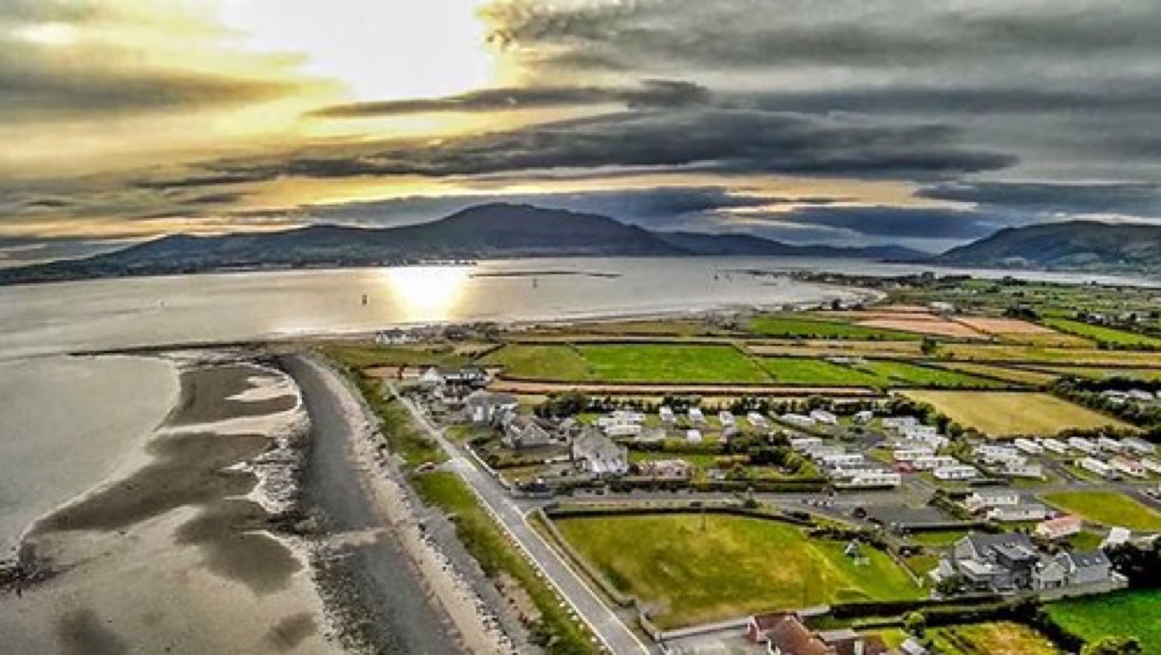 Aerial view over the mouth of Carlingford Lough at Cranfield at dusk, the sun low over the Cooley hills and the village along the shore
