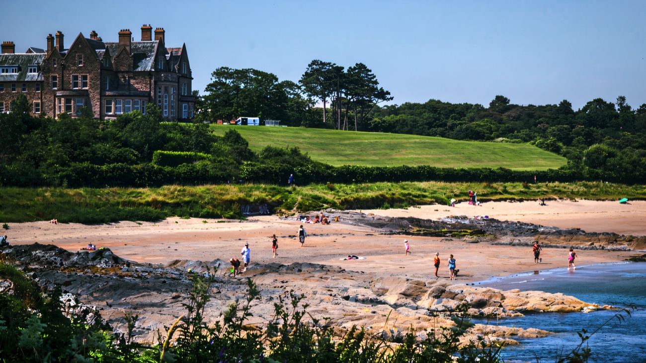 A wide sandy beach at Crawfordsburn framed by trees and green slopes above the shore