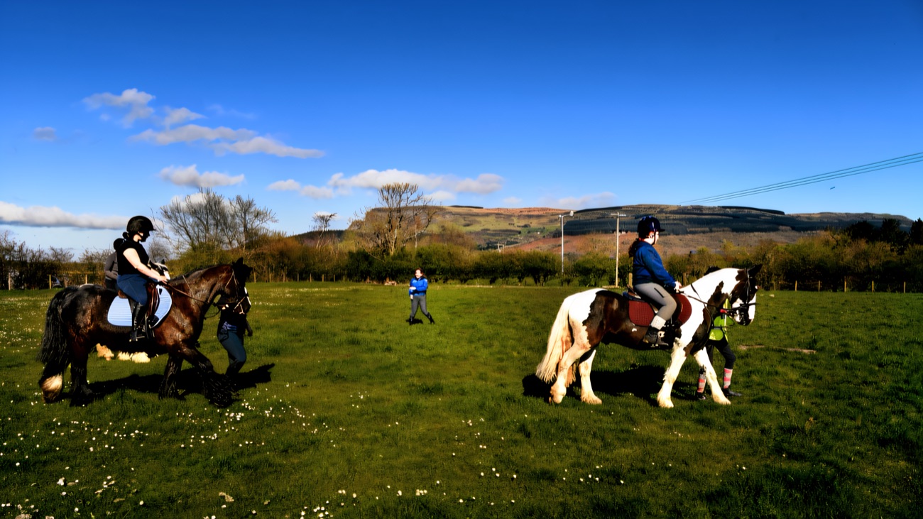 Riders on a countryside trek across a green field with the flat top of Binevenagh Mountain in the distance