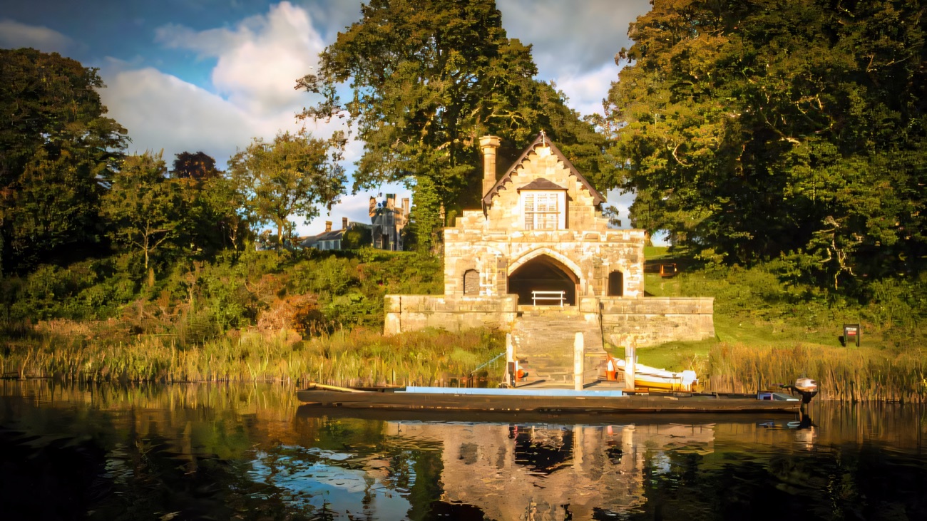 The stone Gothic boathouse at Crom Estate reflected in the lough, with a long wooden boat moored in front