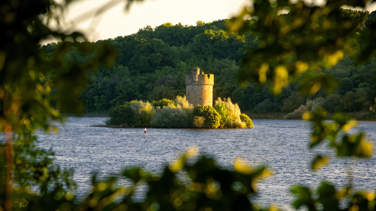 A round stone tower on a small wooded island out in Upper Lough Erne, glowing in evening light