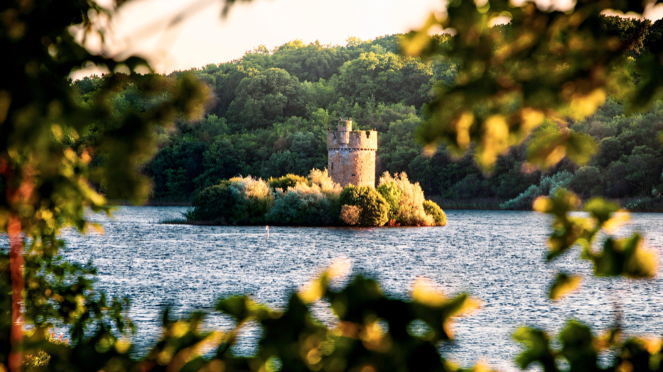 A round stone tower on a small wooded island out in Upper Lough Erne, glowing in the evening light at Crom