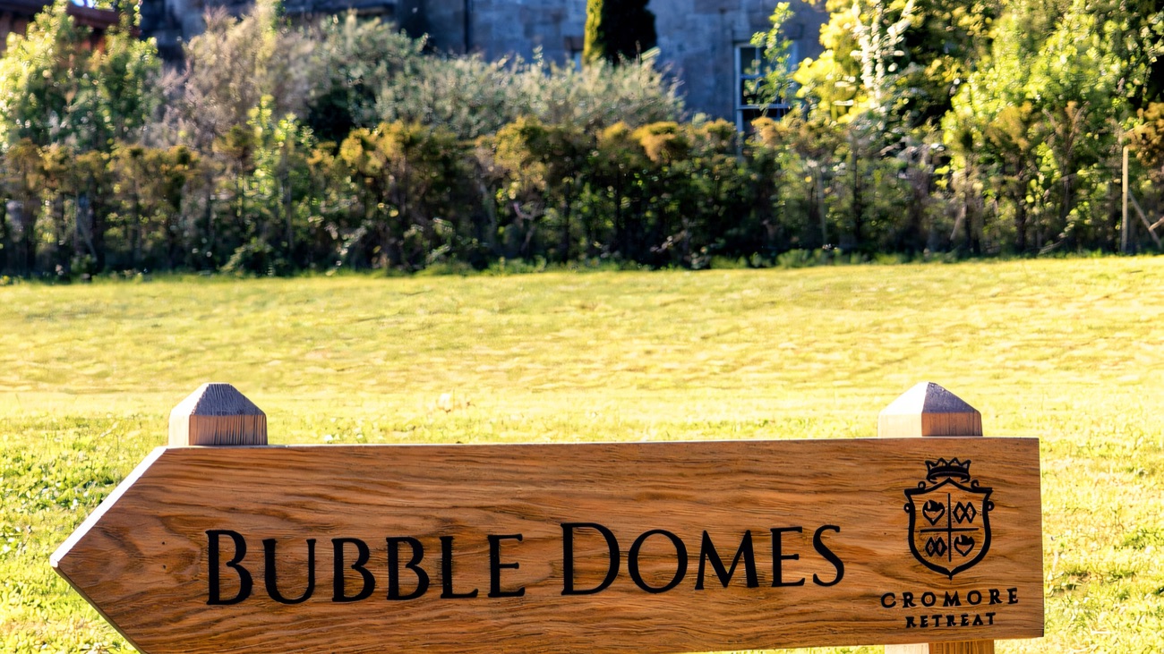 Cromore House behind a lawn, with a wooden estate sign in the foreground for the retreat now on the grounds
