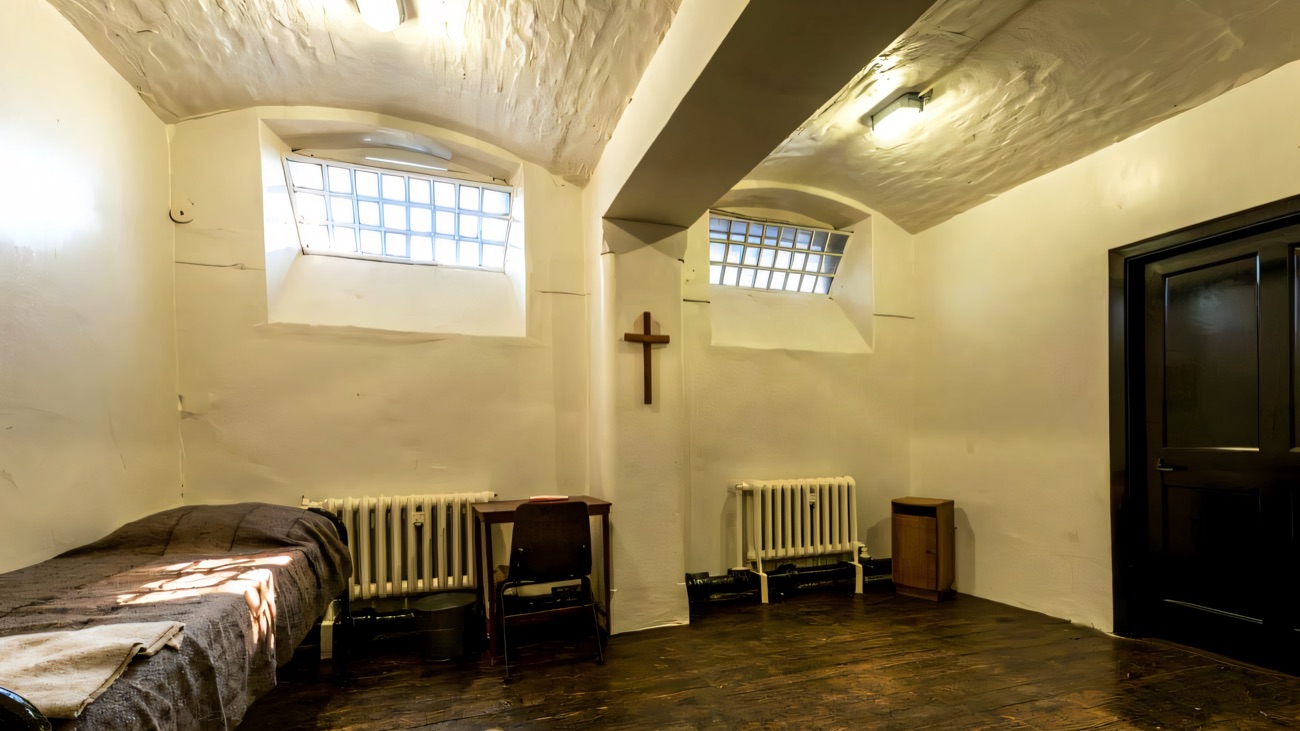 The condemned cell at Crumlin Road Gaol — a plain bed, a cross on the wall and the dark door beside it