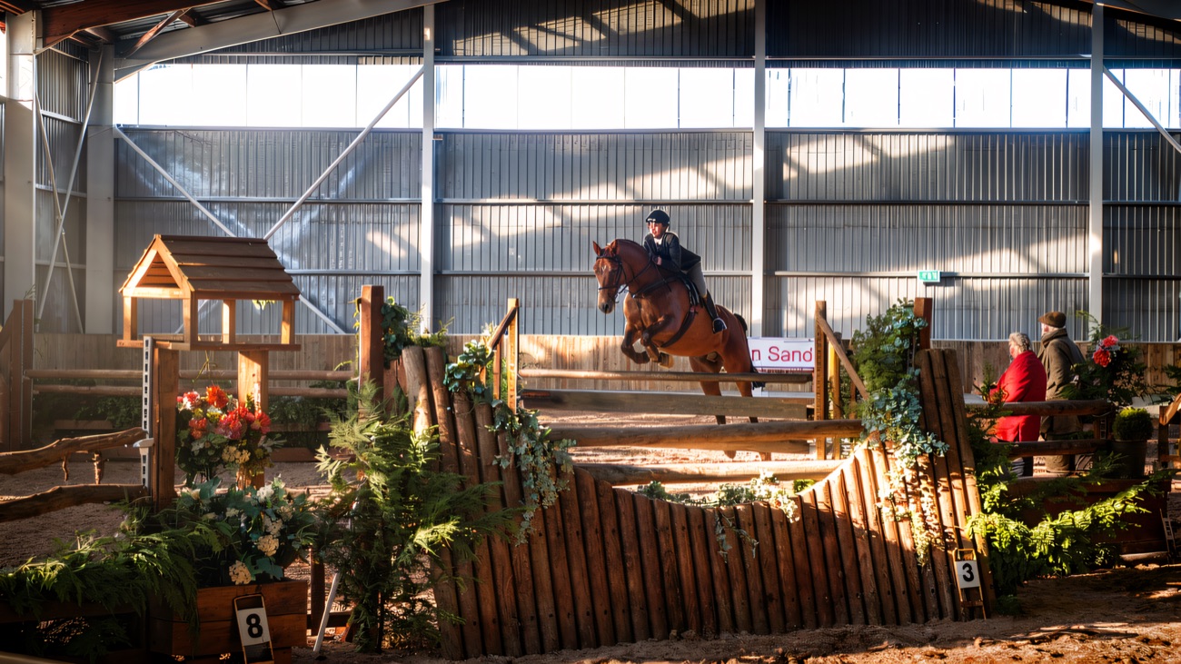 A horse and rider clearing a jump in the floodlit indoor arena