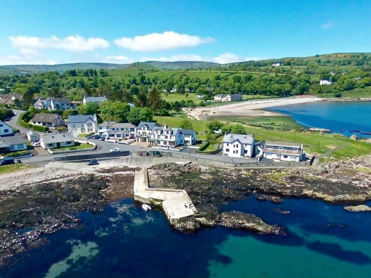 Aerial view of Cushendall harbour and village with its little stone pier, whitewashed houses and the green Glens of Antrim rolling down to Red Bay