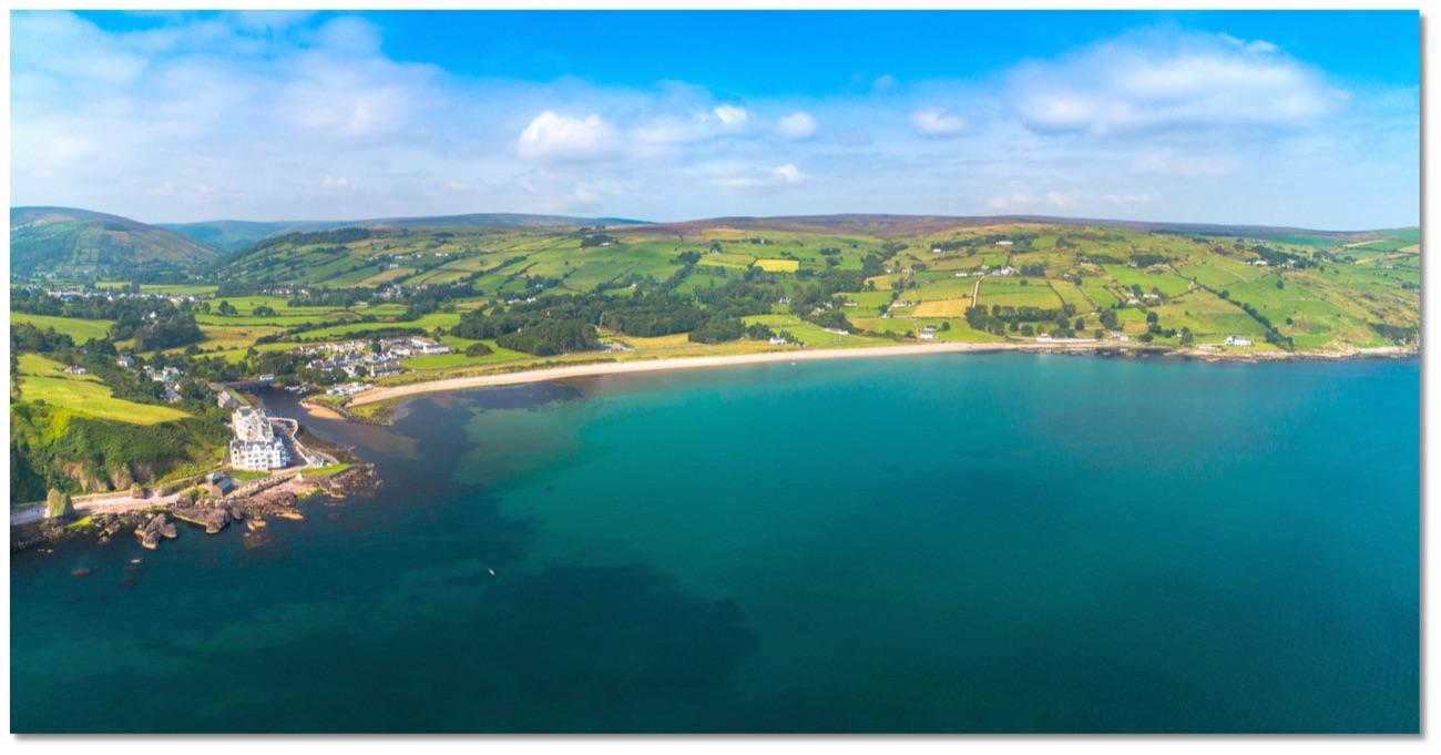 Wide aerial of Cushendun bay, the sandy beach and the patchwork green hills of the Glens of Antrim