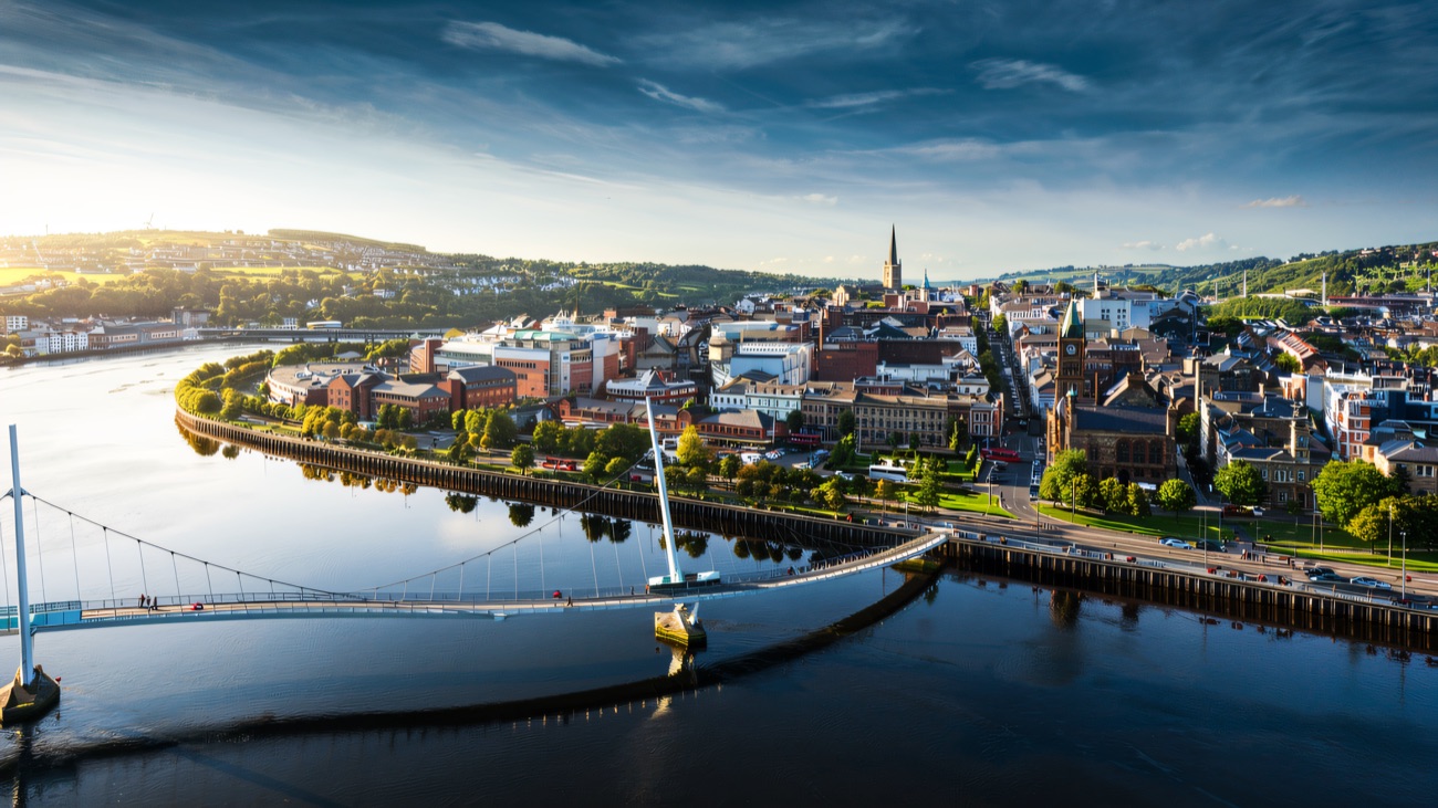 An aerial view over Derry, with the curving Peace Bridge crossing the river into the city