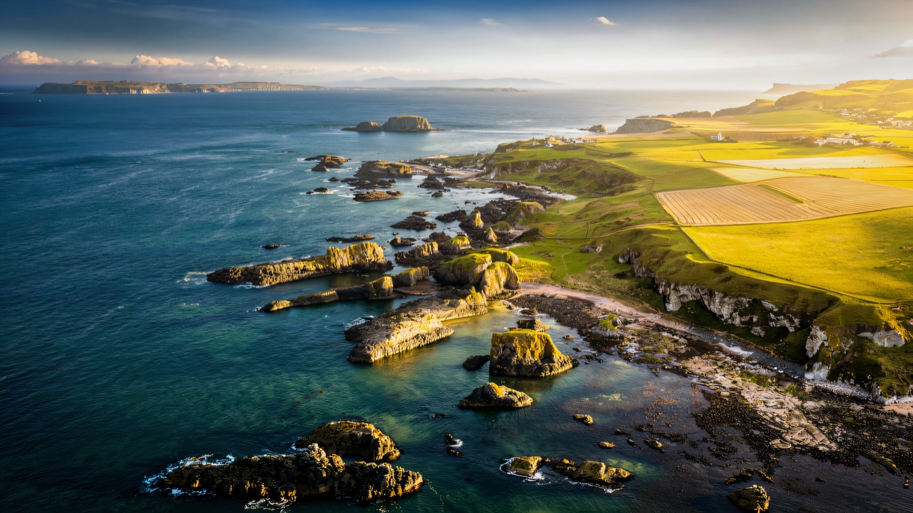 The north coast seen from the air, with dark rocky outcrops in turquoise water and green fields beyond
