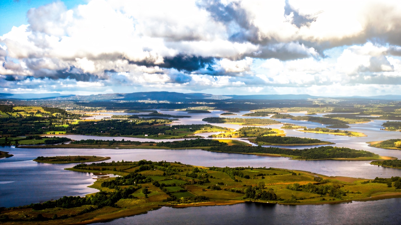 A wide aerial of a lakeland landscape, with green islands scattered across blue water